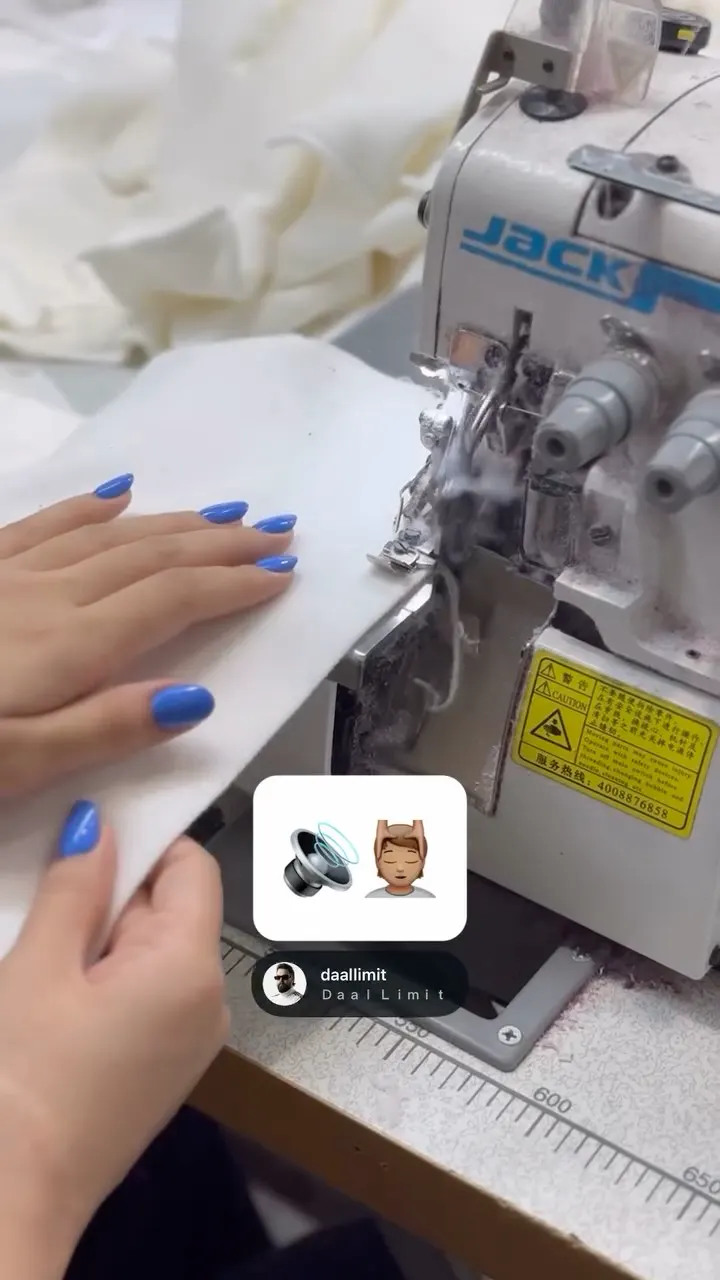دست‌ها در حال دوخت پارچه‌ی سفید با چرخ خیاطی صنعتی